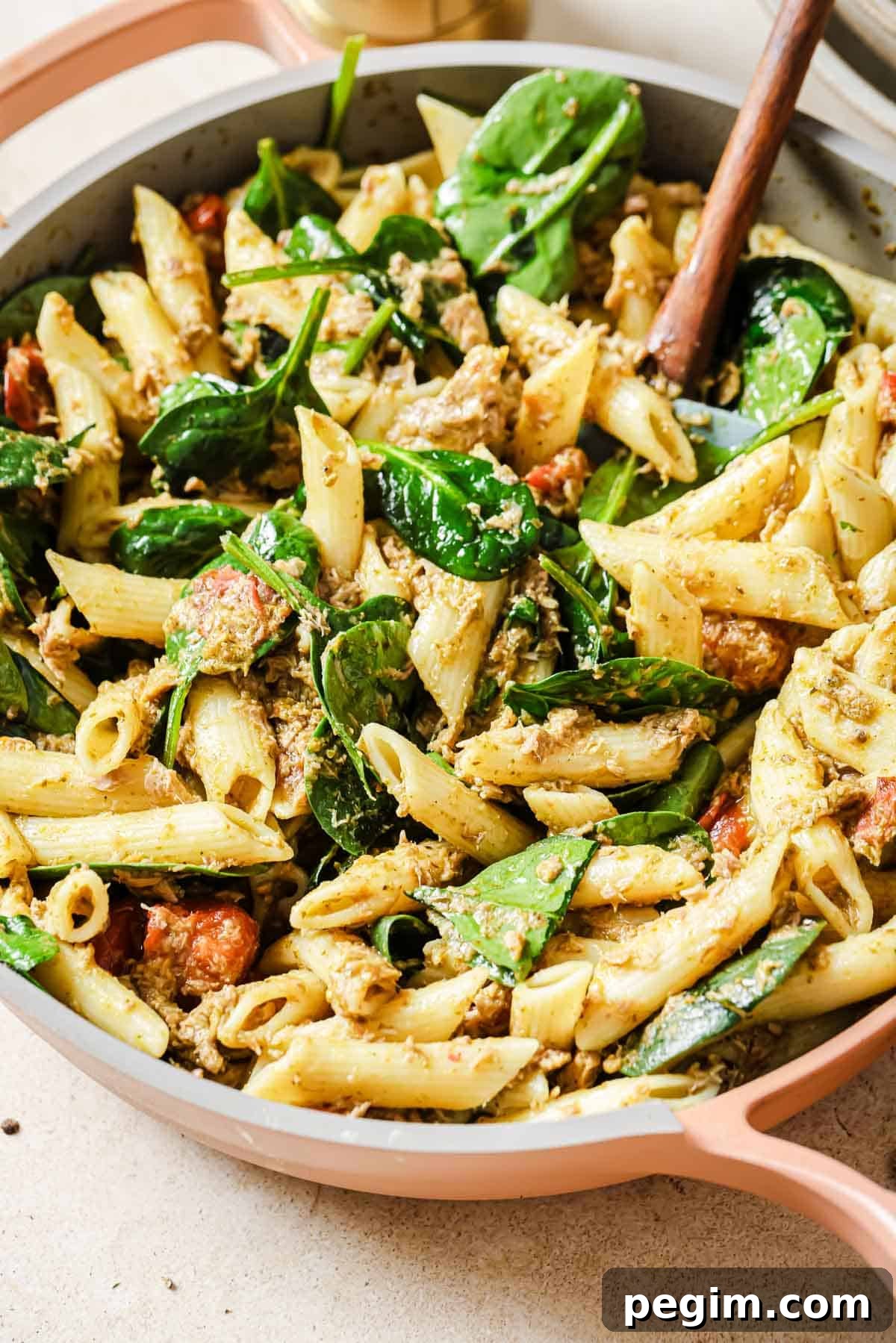 Penne with cherry tomatoes, tuna, spinach and pesto in a skillet.