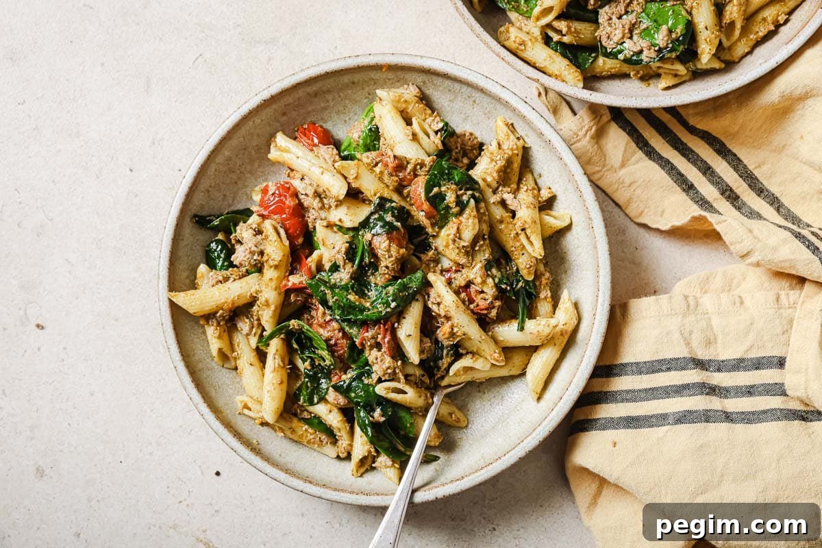 Two bowls of pasta with spinach, tuna, pesto, and cherry tomatoes.
