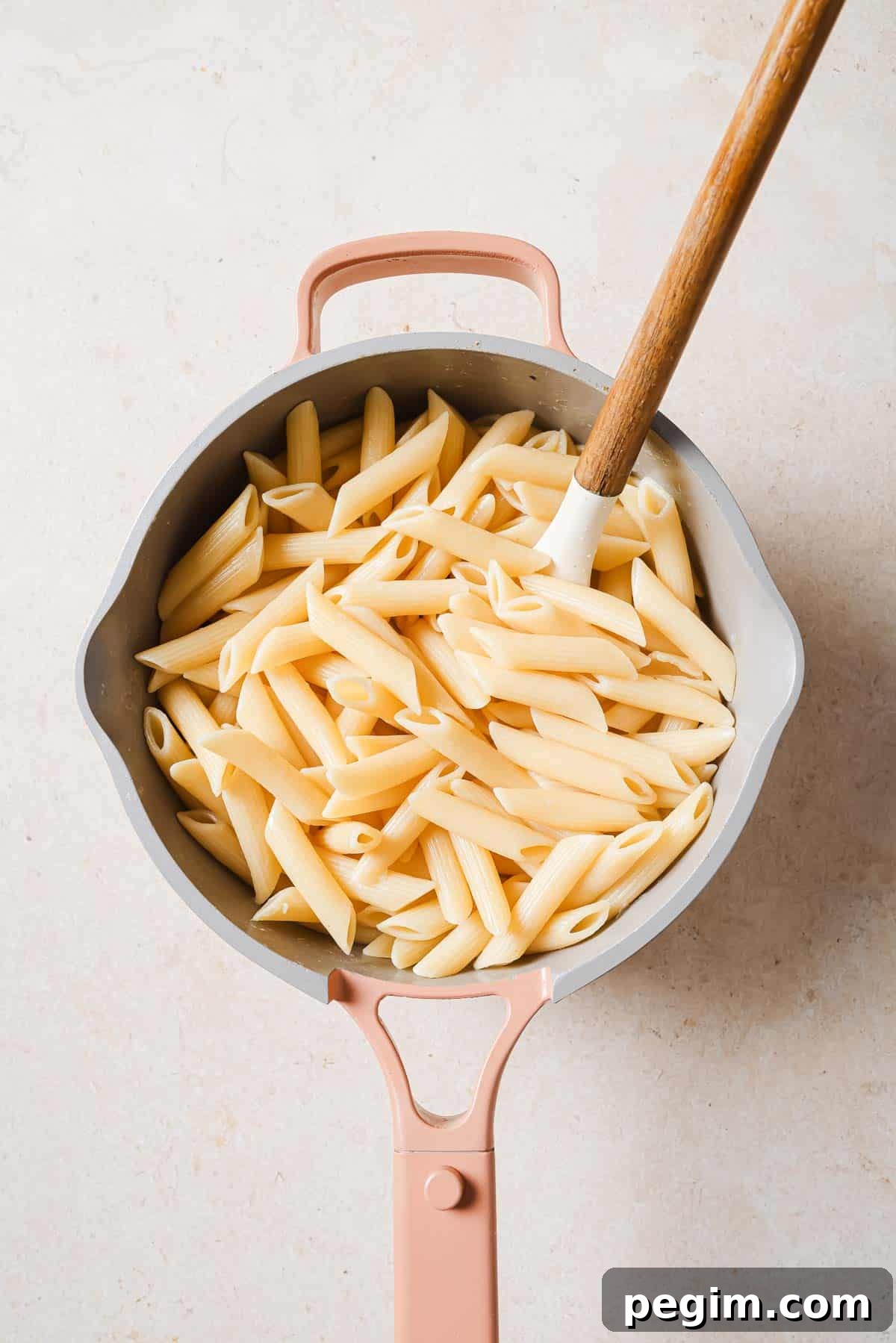 Penne pasta in a pan with a wooden spoon.