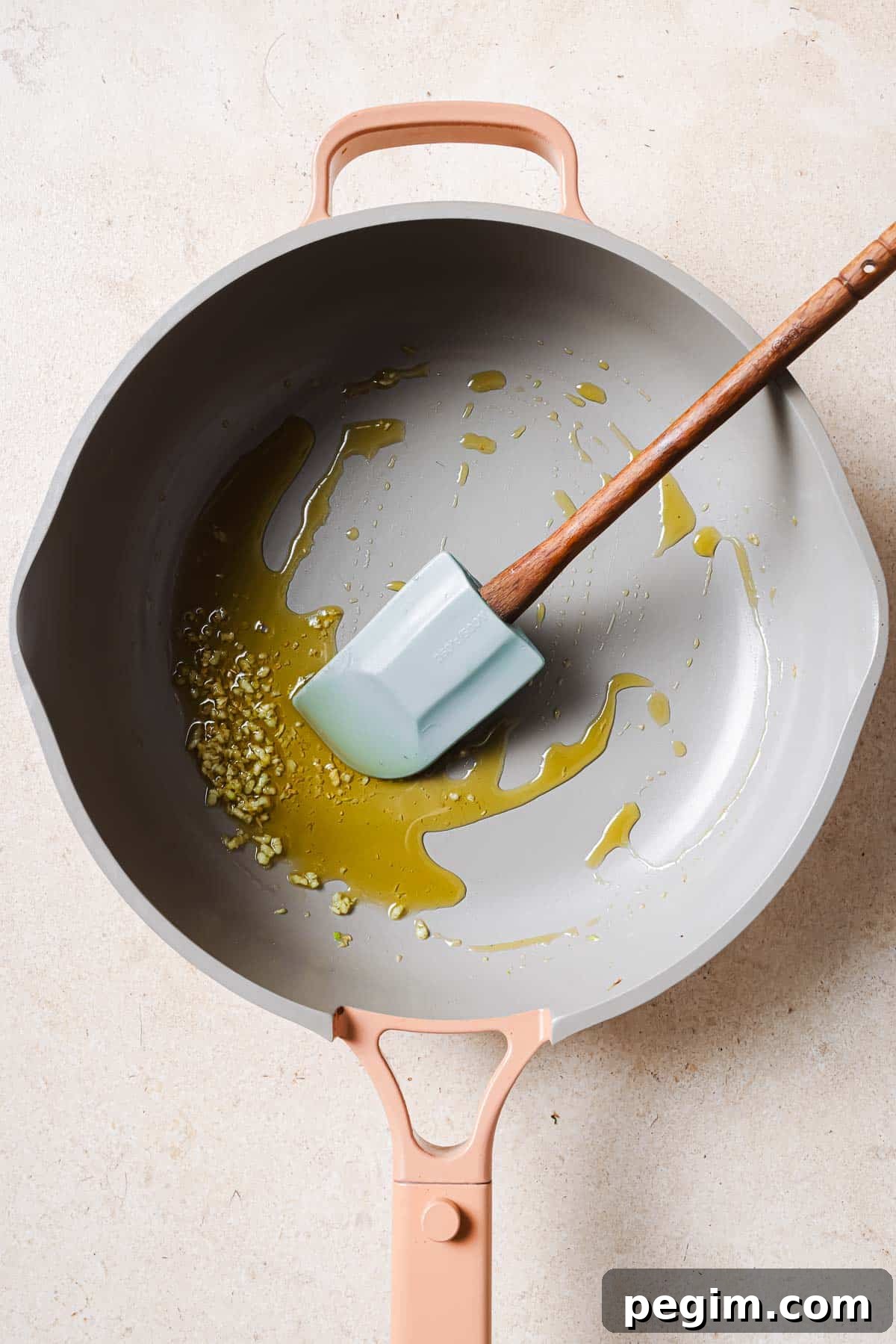 A frying pan with olive oil, garlic, and a wooden spatula.