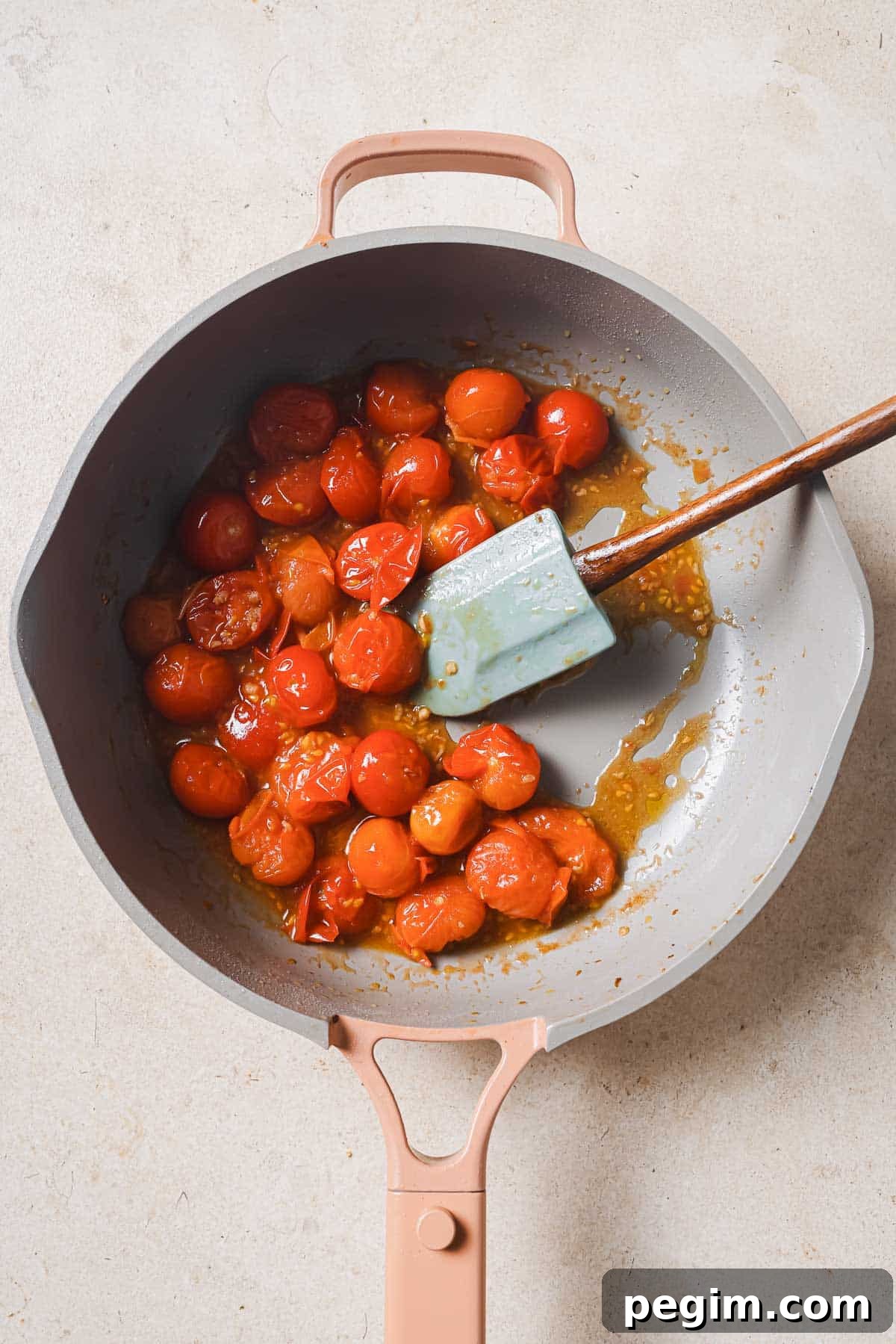 A frying pan with tomatoes and a wooden spatula.