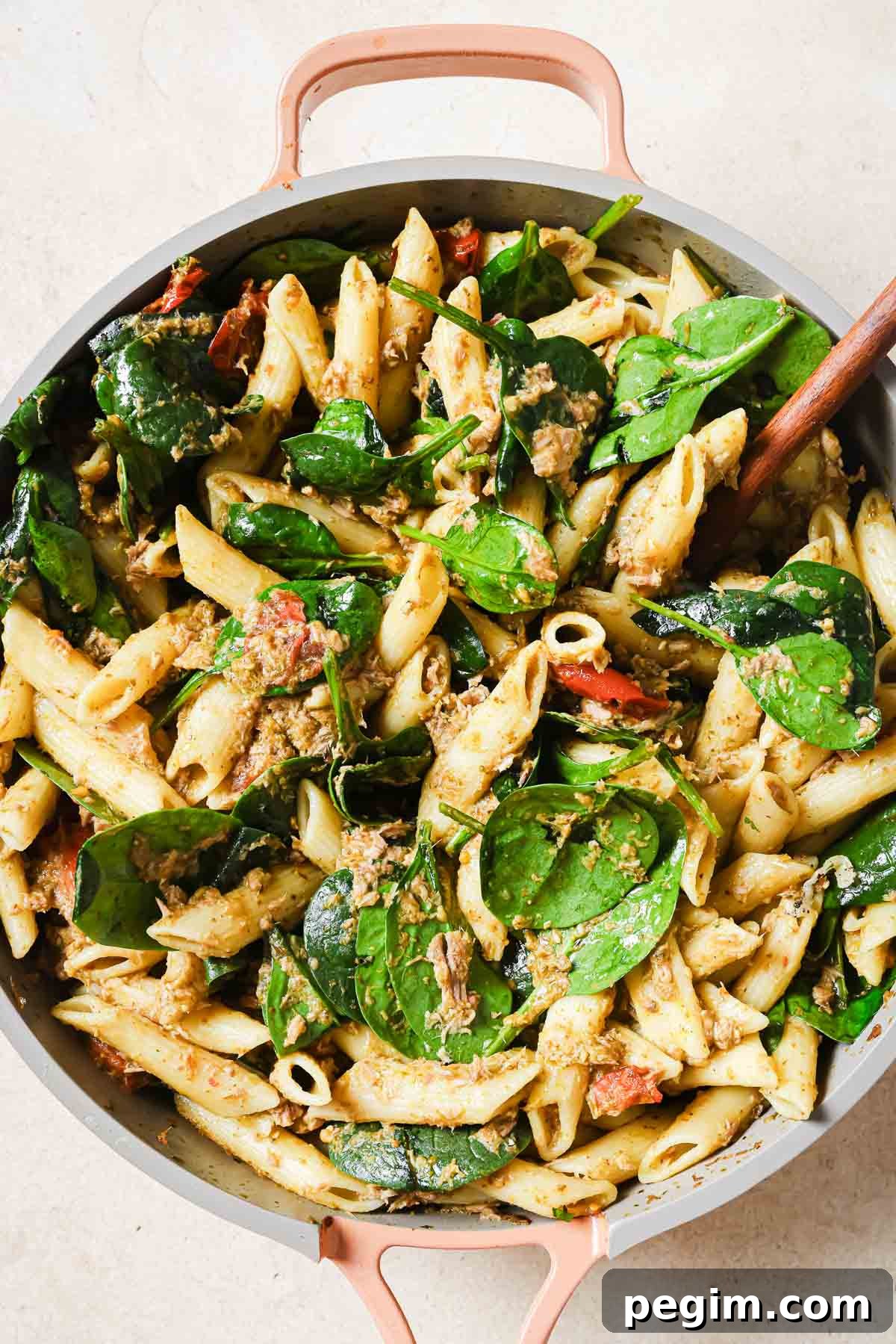 A pan full of tuna pesto pasta with a wooden spoon.