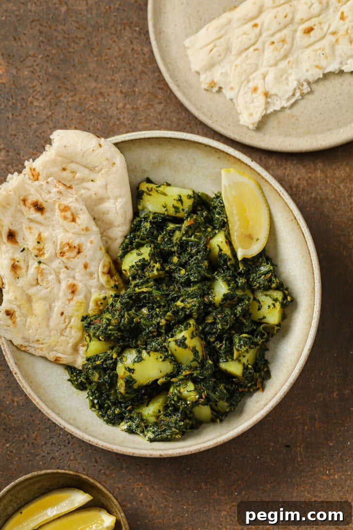 A plate of Aloo Palak with naan and a lemon wedge.