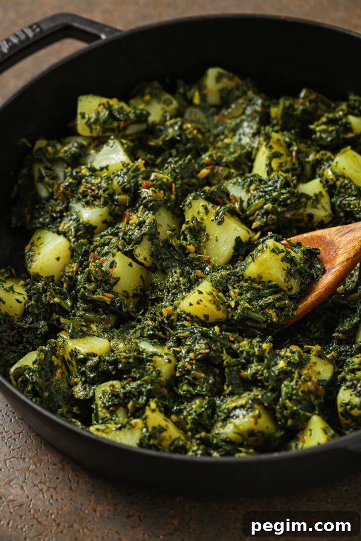 Close up of Aloo Palak in a skillet with a wooden spoon.