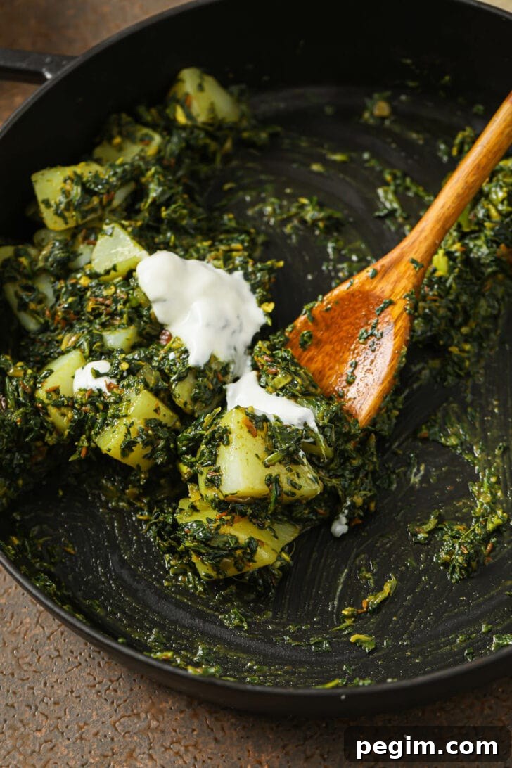 Close up of Aloo Palak in skillet topped with dollops of yogurt.
