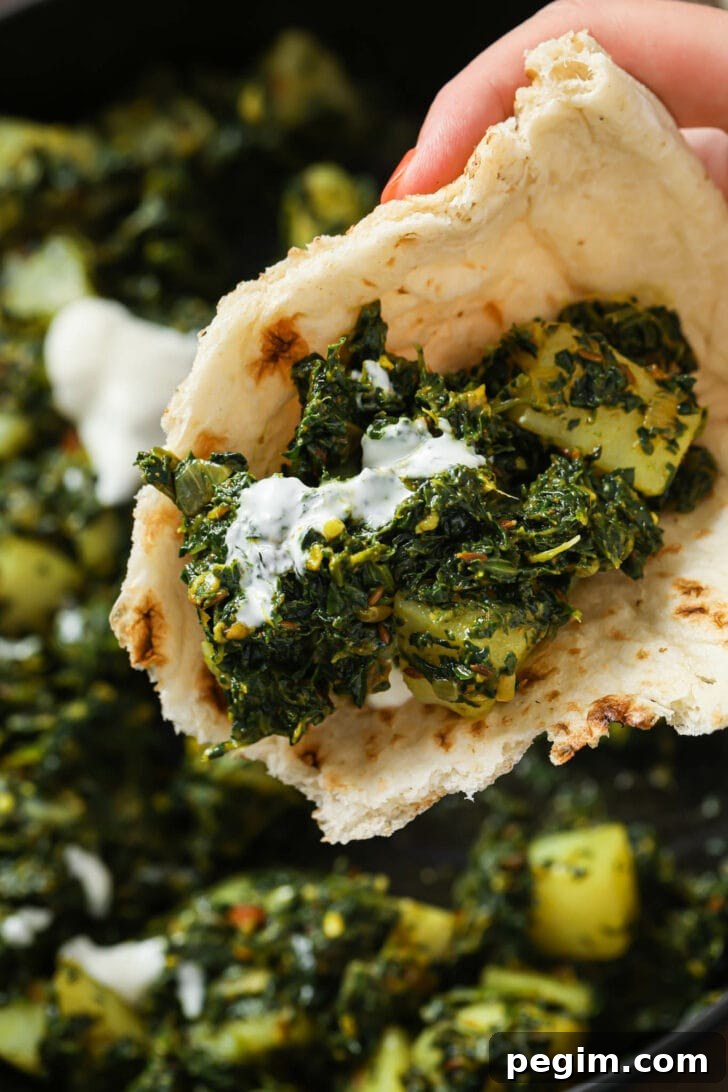 Holding some Aloo palak with yogurt in a piece of naan.