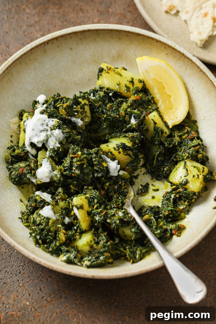 Aloo palak in a bowl with some yogurt and a fork.