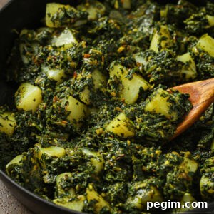 Close up of Aloo Palak in a skillet with a wooden spoon.