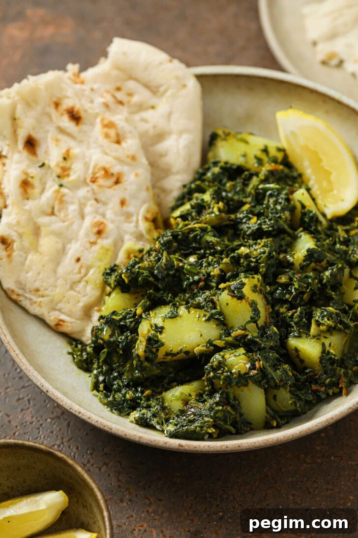 A plate of Aloo Palak with naan and a lemon wedge.