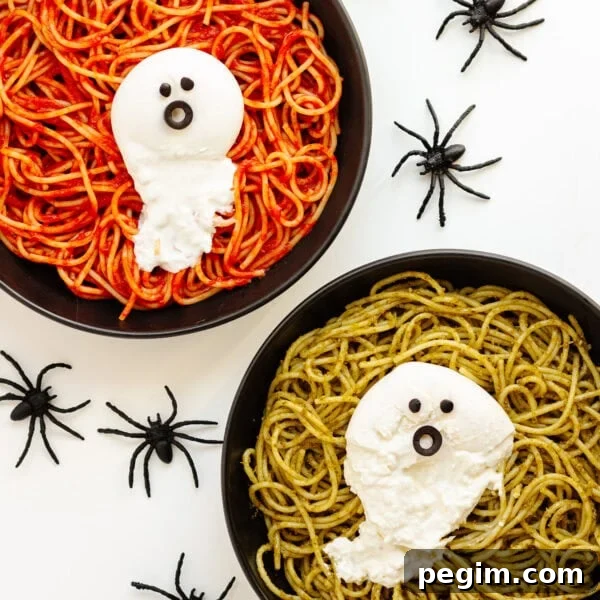 Two plates of spaghetti (one with tomato sauce and one with pesto) topped with burrata ghosts and surrounded by spiders.