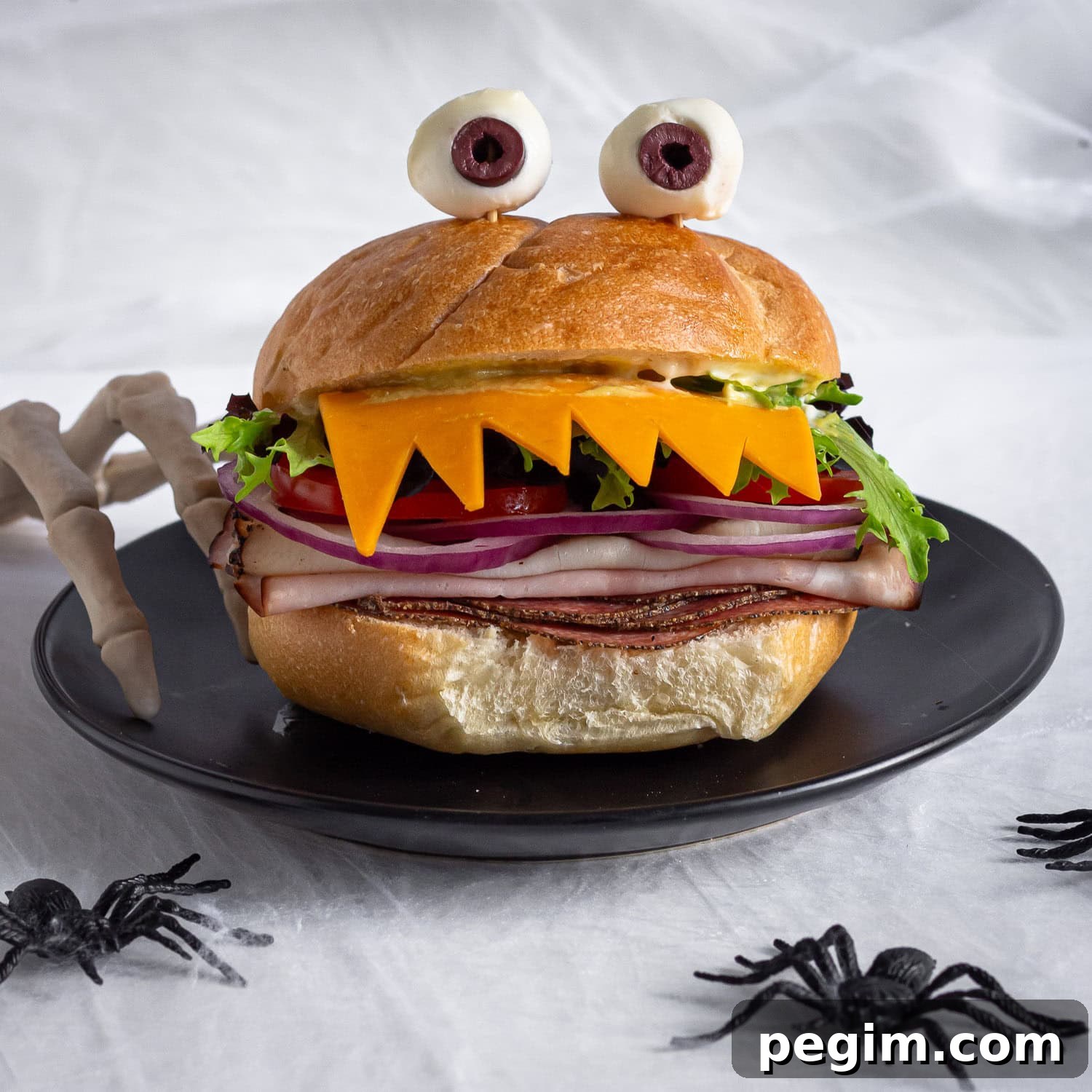 Spooky monster sandwich on a black plate with Halloween decorations around it.