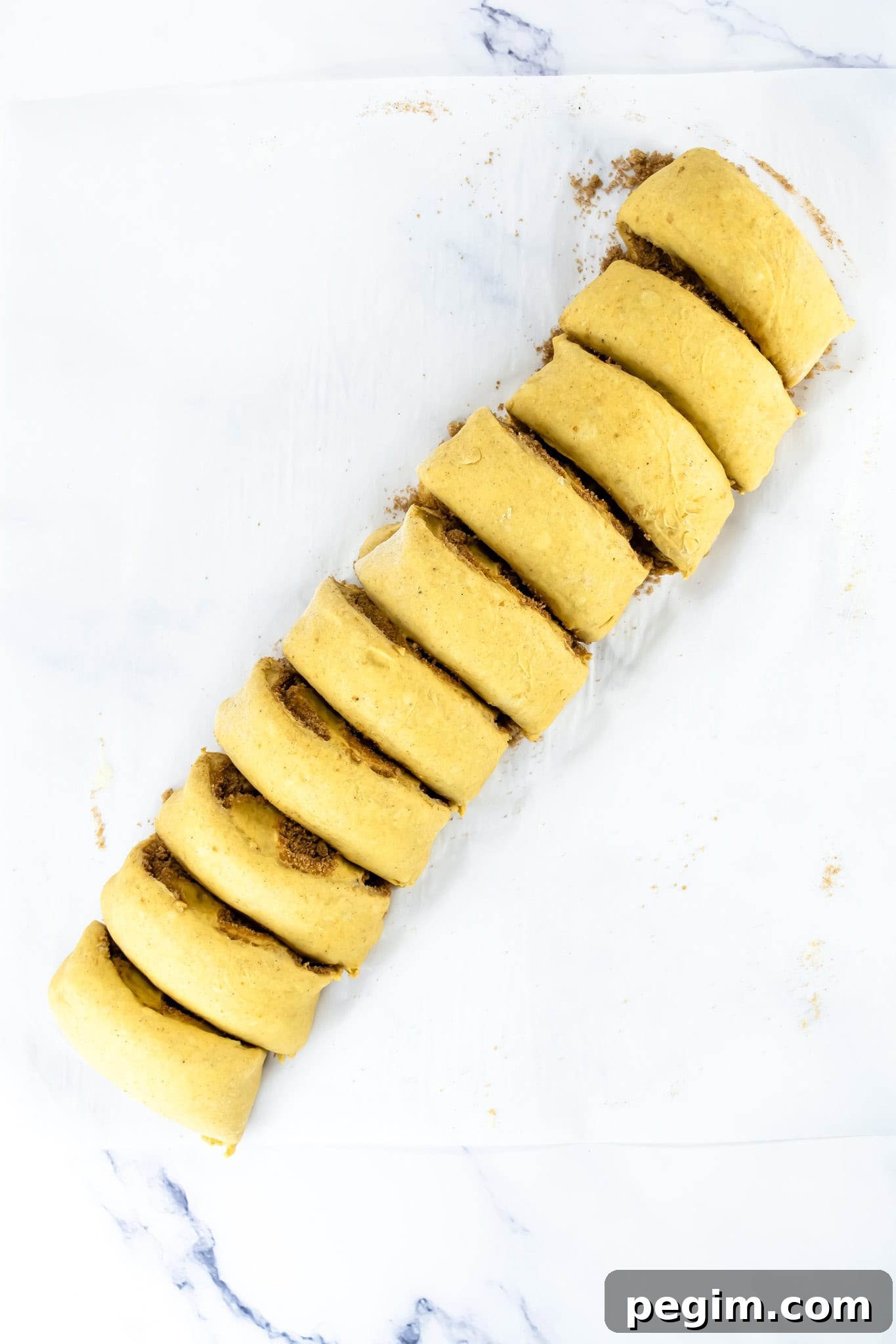 Sliced unbaked Pumpkin Cinnamon Rolls dough arranged on parchment paper, ready for baking.