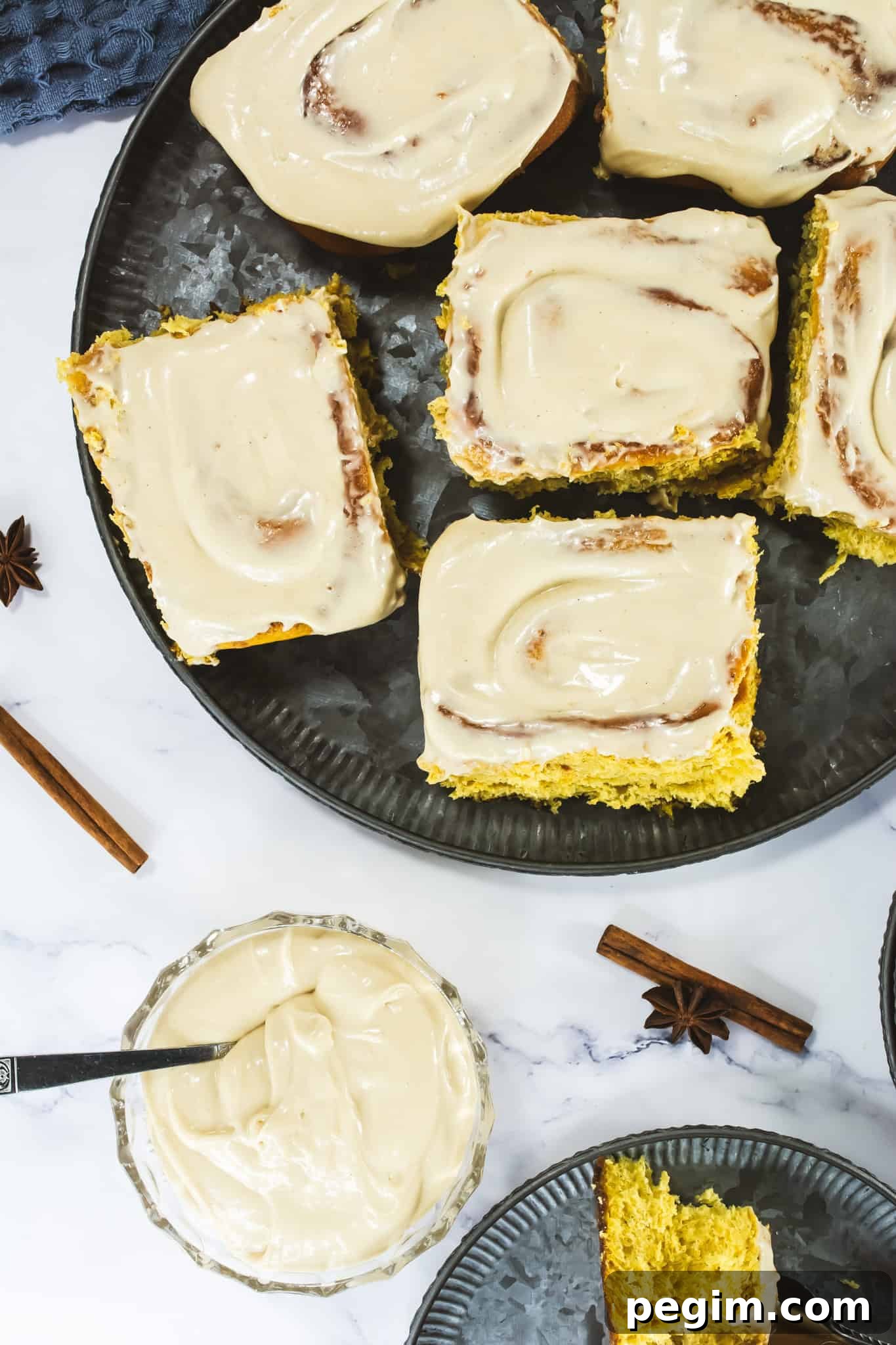 Cream cheese frosting spread over a freshly baked pumpkin sheet cake with cinnamon and nutmeg, topped with white icing, on a black serving platter. Perfect for fall baking and holiday desserts.