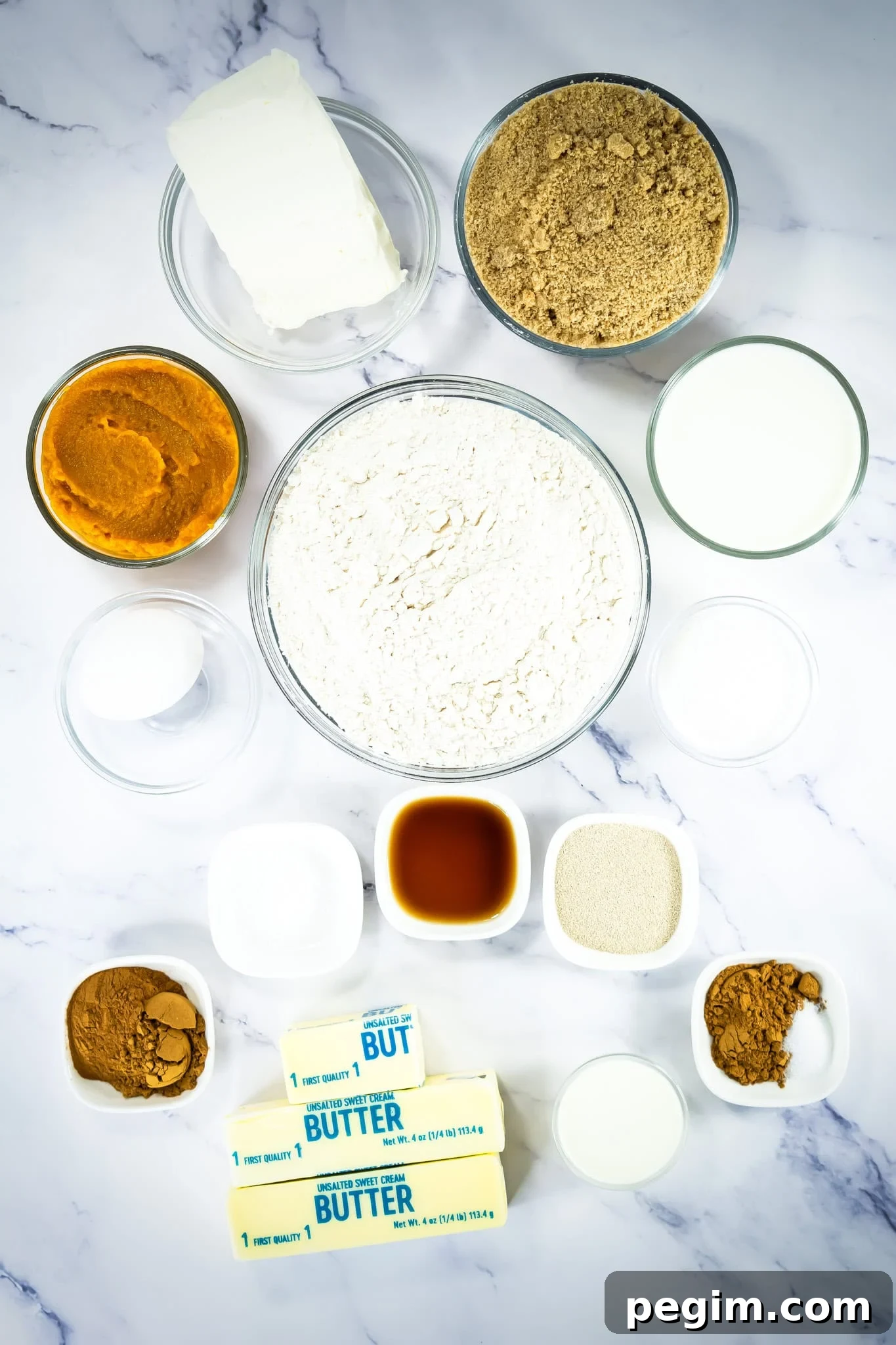 Assorted baking ingredients—flour, butter, pumpkin puree, brown sugar, spices, milk, and more—on a marble surface