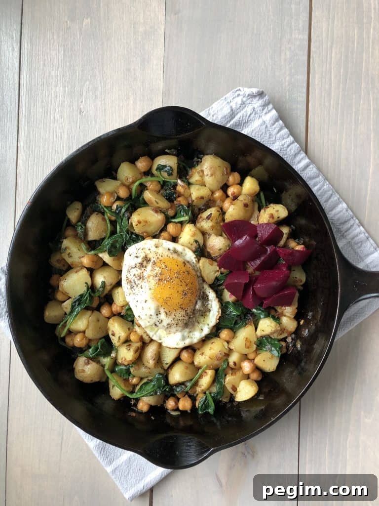 A skillet filled with pytt i panna, a fried egg and pickled beets on a kitchen towel