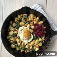 A skillet filled with pytt i panna, a fried egg and pickled beets on a kitchen towel