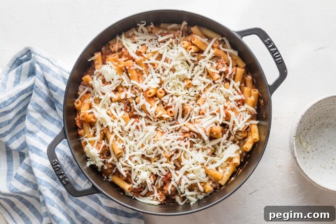 Shredded mozzarella sprinkled on top of a pasta dish, ready to bake.