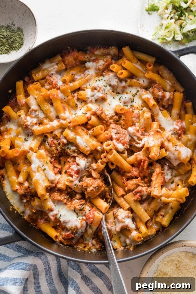 Large cast iron skillet filled with baked ziti with Italian sausage, ready to serve.