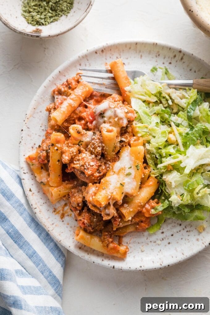 Small plate with a serving of baked ziti and Caesar salad.