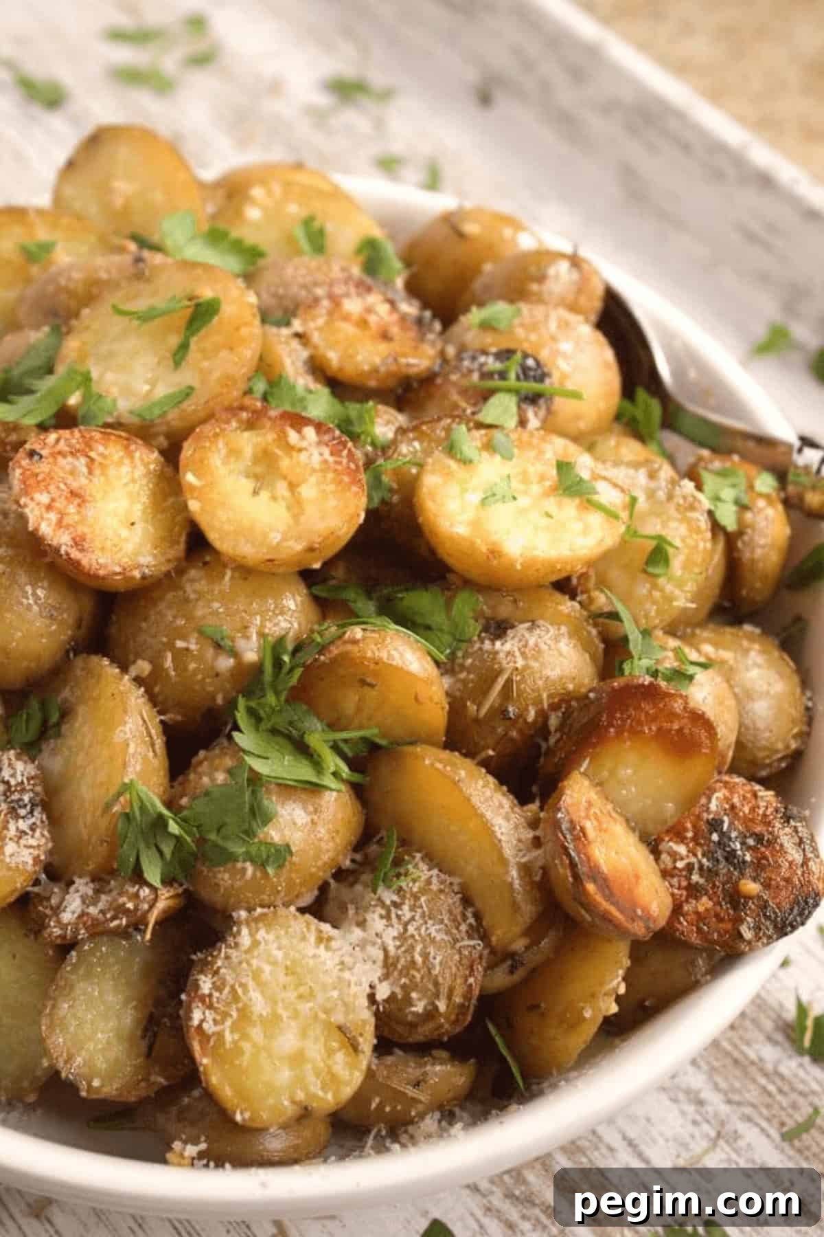 A bowl of sliced, roasted Crock Pot red potatoes garnished with grated cheese and fresh parsley.