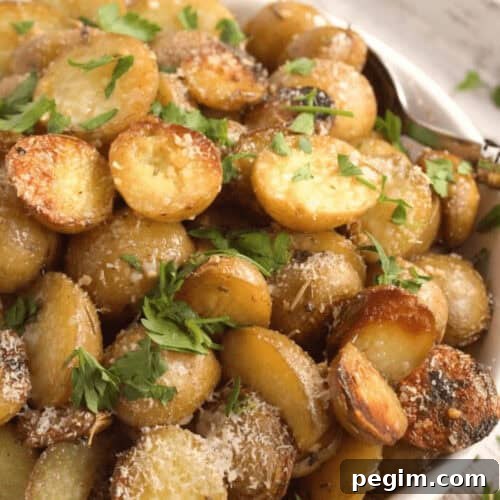A bowl of sliced, roasted Crock Pot red potatoes garnished with grated cheese and fresh parsley.