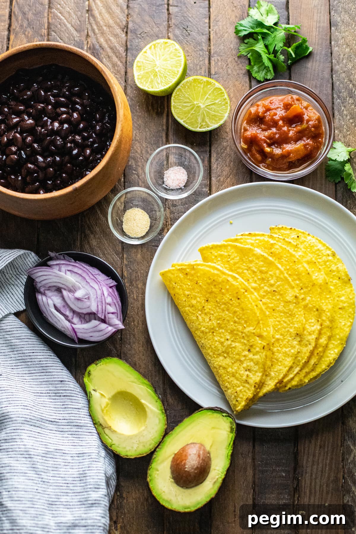 Ingredients for black bean tacos arranged on wooden background.