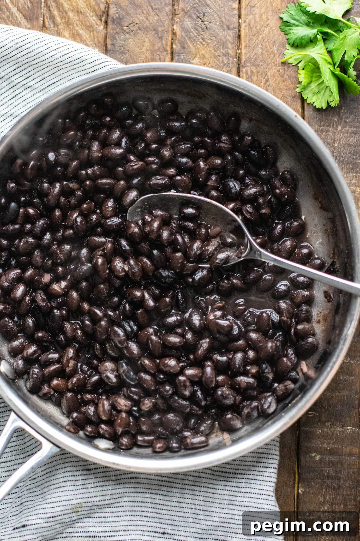 black beans cooking in stainless steel pan with spoon mixing.
