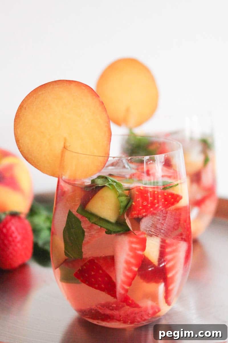 Close-up sideview of one glass of sparkling rose sangria garnished with a peach round with a second glass in the background.