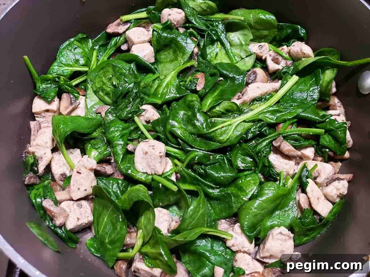 wilted spinach, chicken, and mushrooms cooking in a pan