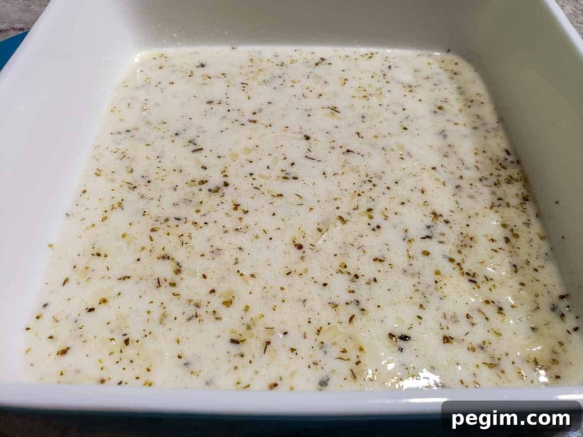 an 8x8 inch casserole dish with white sauce layered on the bottom