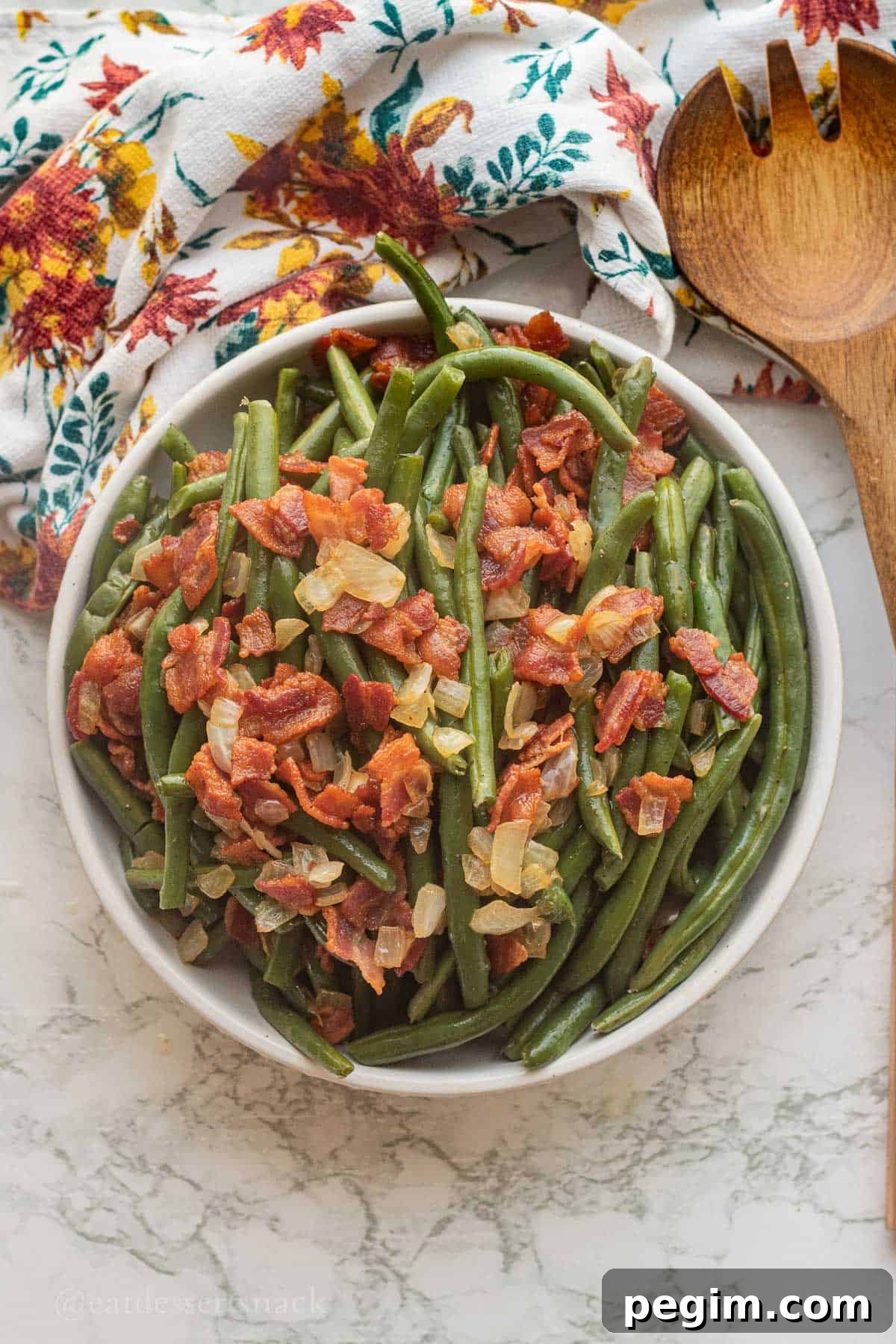 Bacon and onion on bowl of cooked green beans with wooden spoon.