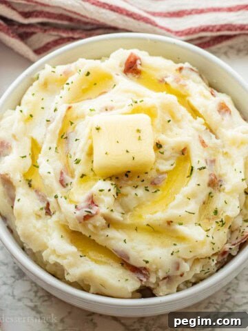 Red skin mashed potatoes with butter on top in white bowl.