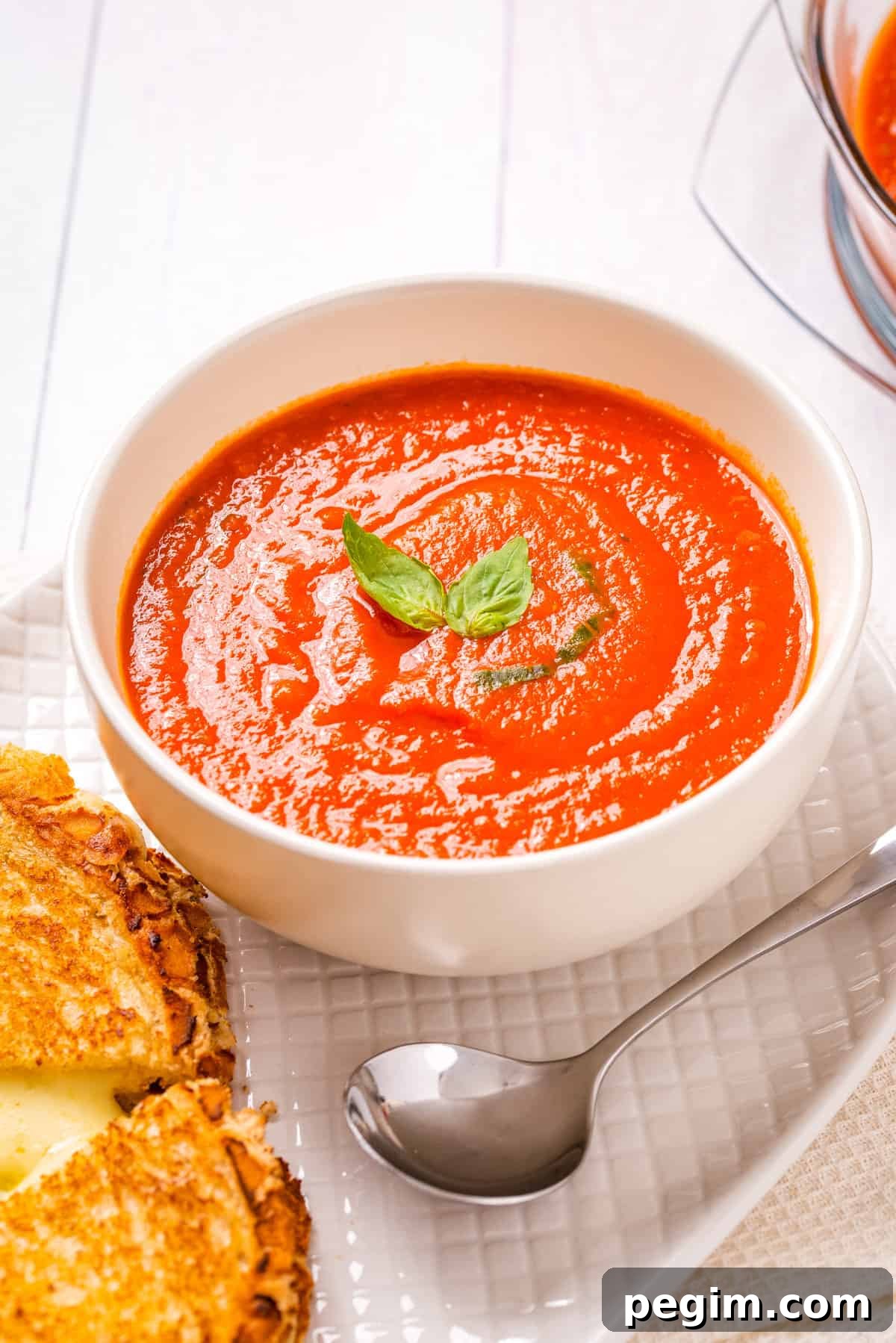 Overhead view of instant pot tomato soup in a white bowl with cheese toasties on the side and a spoon. 