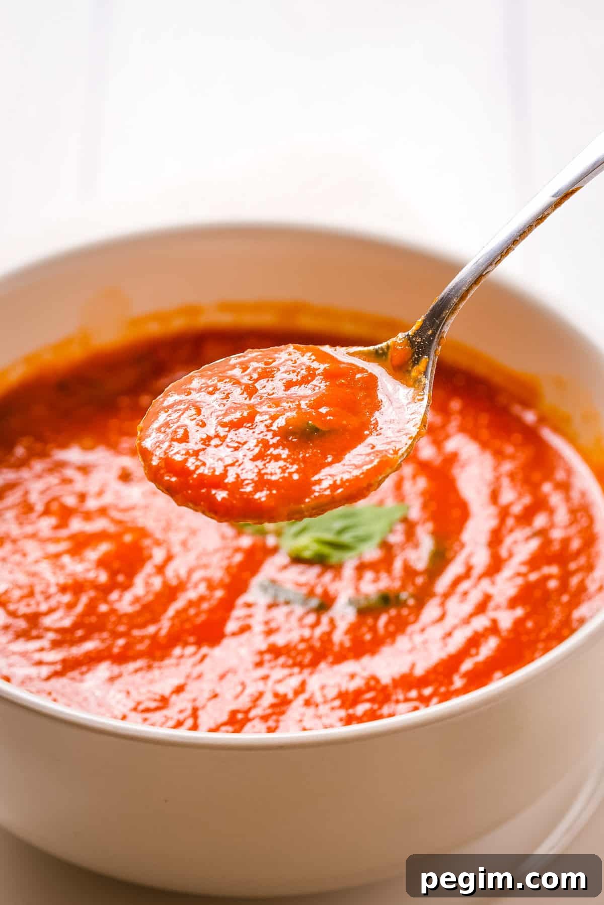Close up shot of tomato soup in white bowl with a spoon lifting some soup out.