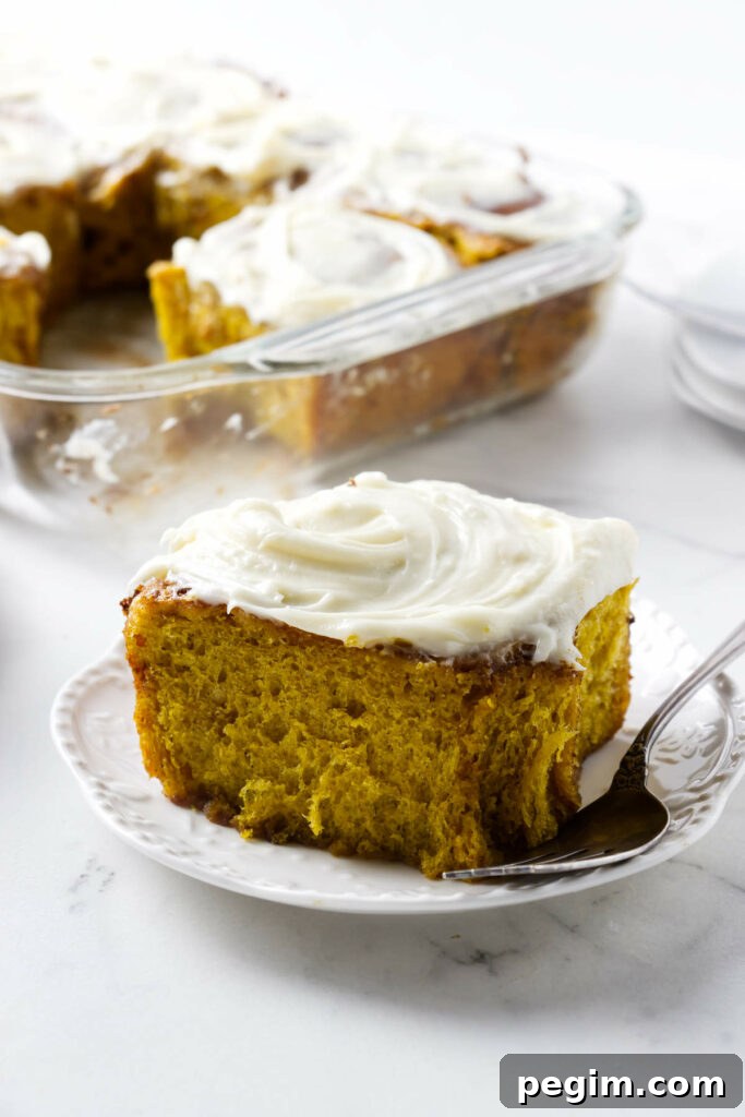 A plate with a pumpkin cinnamon bun in front of a dish with more rolls.