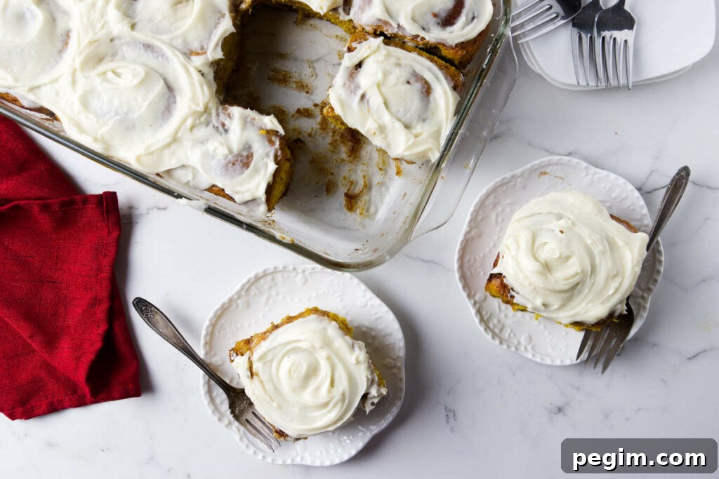 Two pumpkin rolls topped with cream cheese frosting next to a dish with more buns.