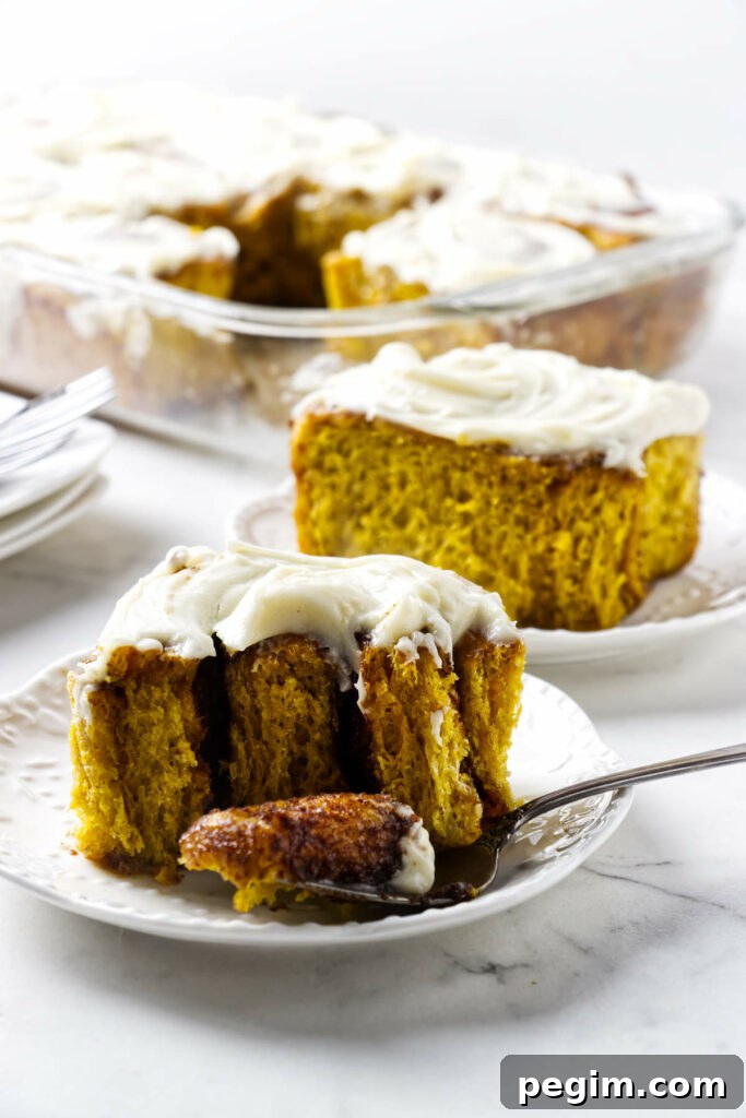 Frosted pumpkin cinnamon rolls on a plate with more rolls in background.