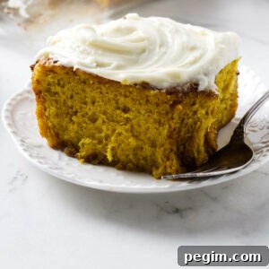 A pumpkin cinnamon roll on a dessert plate topped with cream cheese icing.