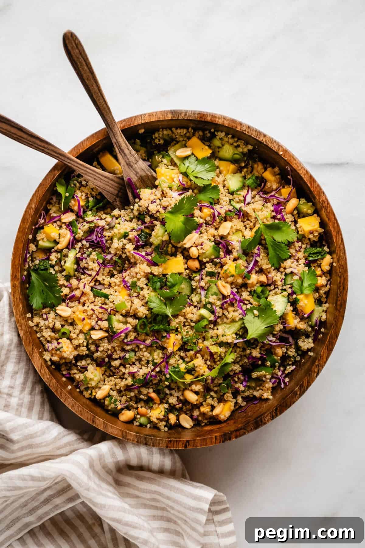 Thai quinoa salad in a wood salad bowl with wooden serving spoons.