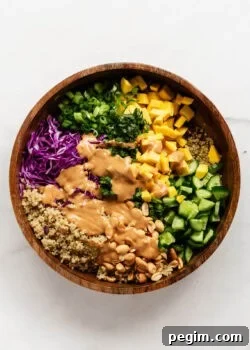 Thai quinoa salad in a wood salad bowl with peanut dressing poured over it.