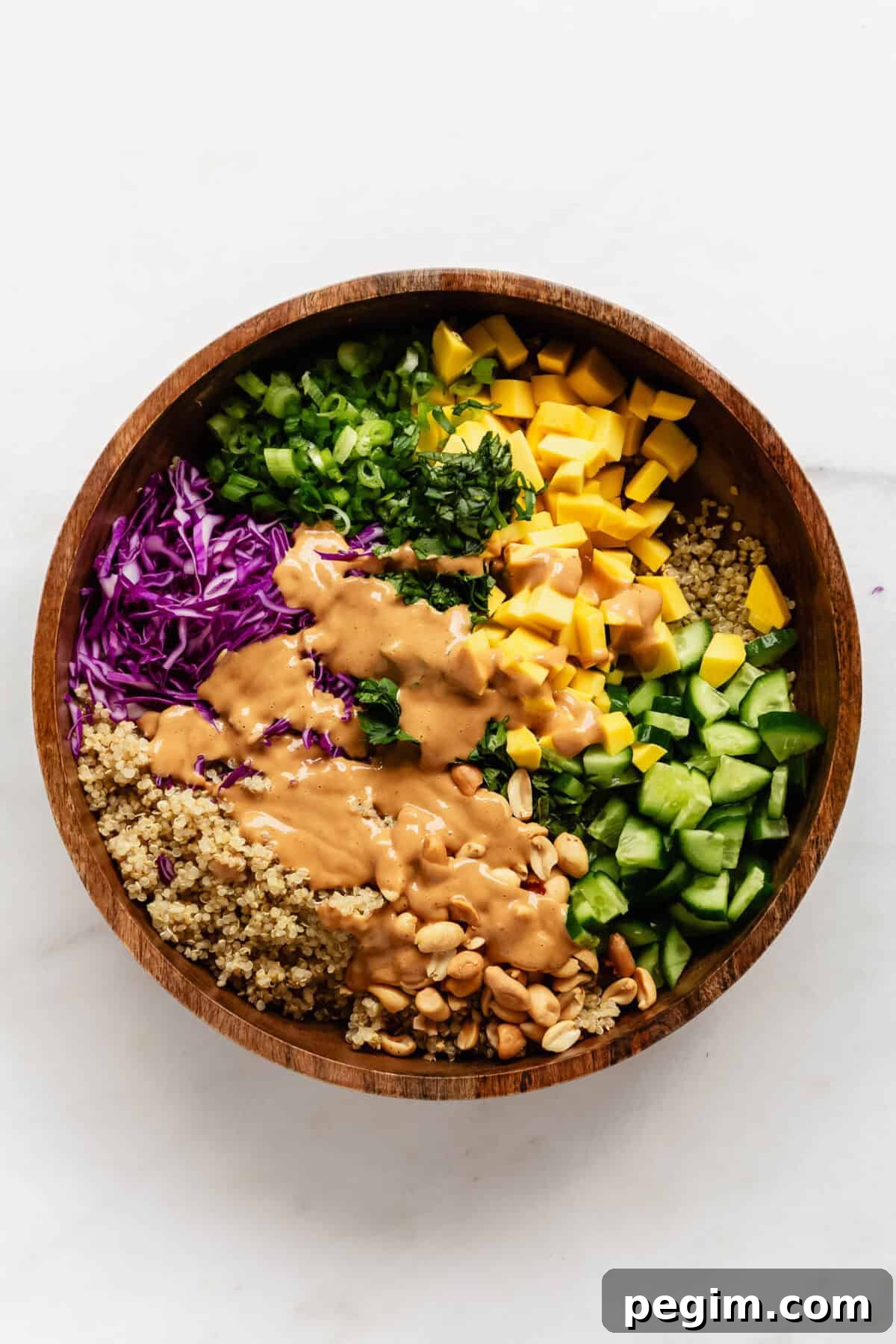 Thai quinoa salad in a wood salad bowl with peanut dressing poured over it.