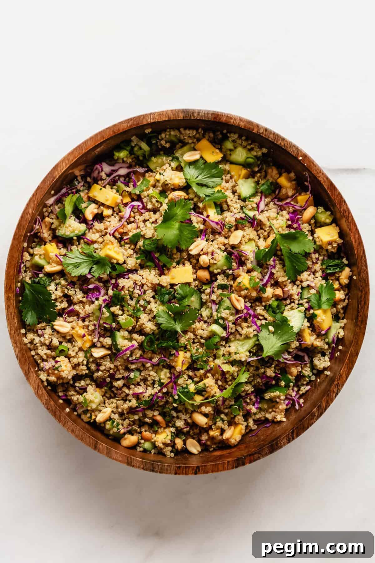 Thai quinoa salad in a wood mixing bowl topped with cilantro leaves.