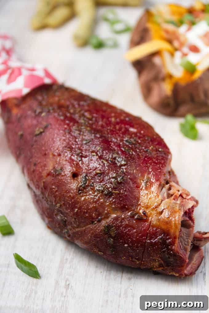 Smoked wild turkey leg laying on white cutting board with loaded baked sweet potatoes and some fried green beans