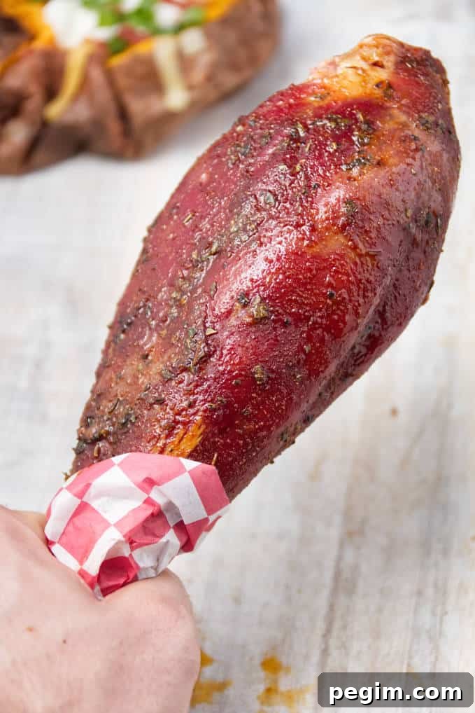 Smoked wild turkey leg laying on white cutting board with loaded baked sweet potatoes