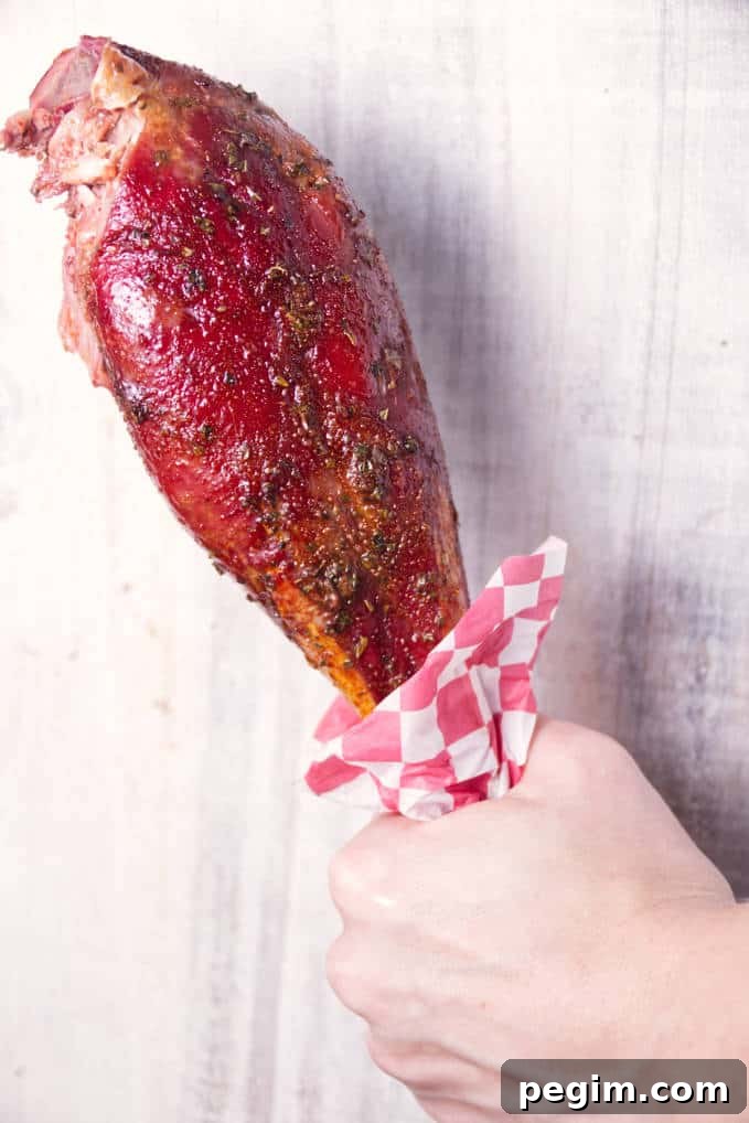 Smoked wild turkey leg being held with a red and white checkered deli paper