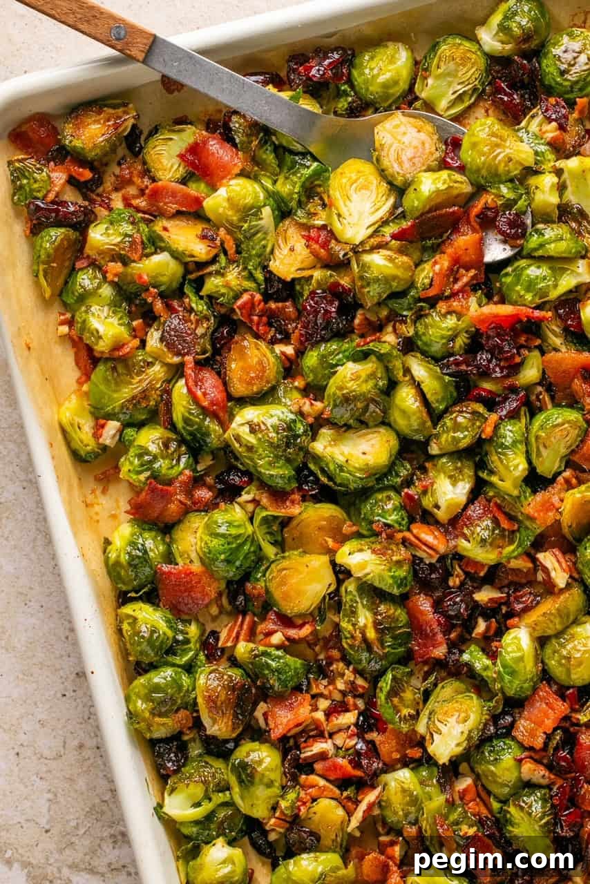 a spoon lifting maple bacon brussels sprouts off of a baking sheet
