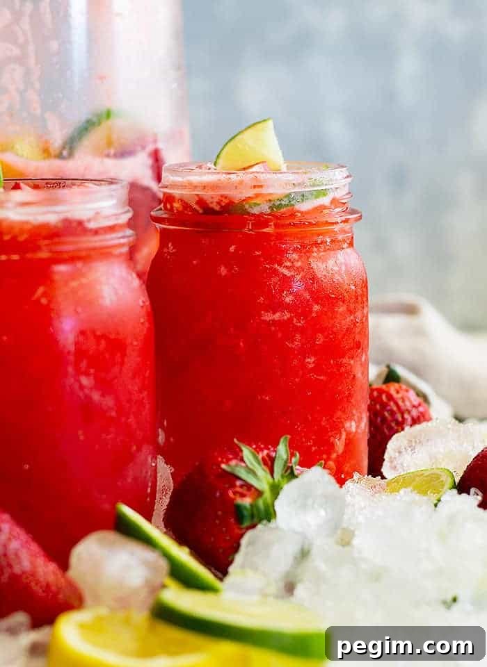 two glasses of strawberry lemonade with ice, fresh strawberries, and lime slices