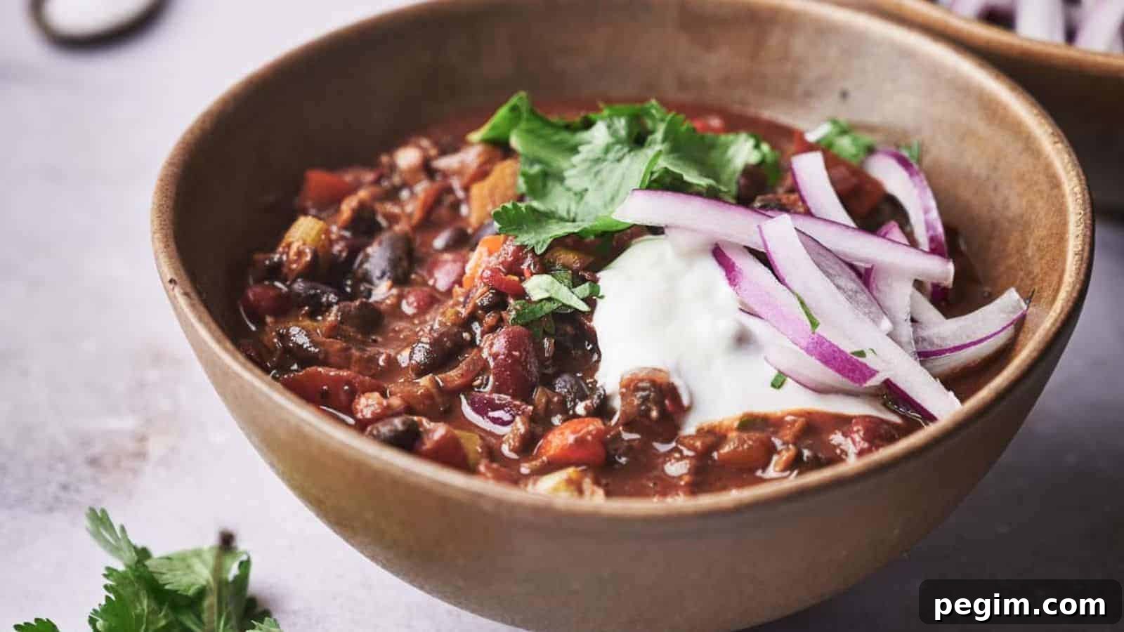 Two bowls of chili with onions and sour cream.