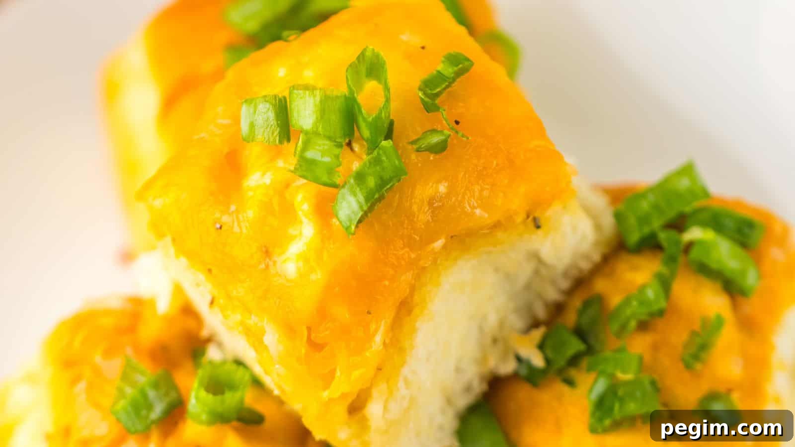 Close-up of cheesy garlic bread rolls topped with chopped green onions on a white plate, reminiscent of Loaded Buffalo Chicken Rolls.