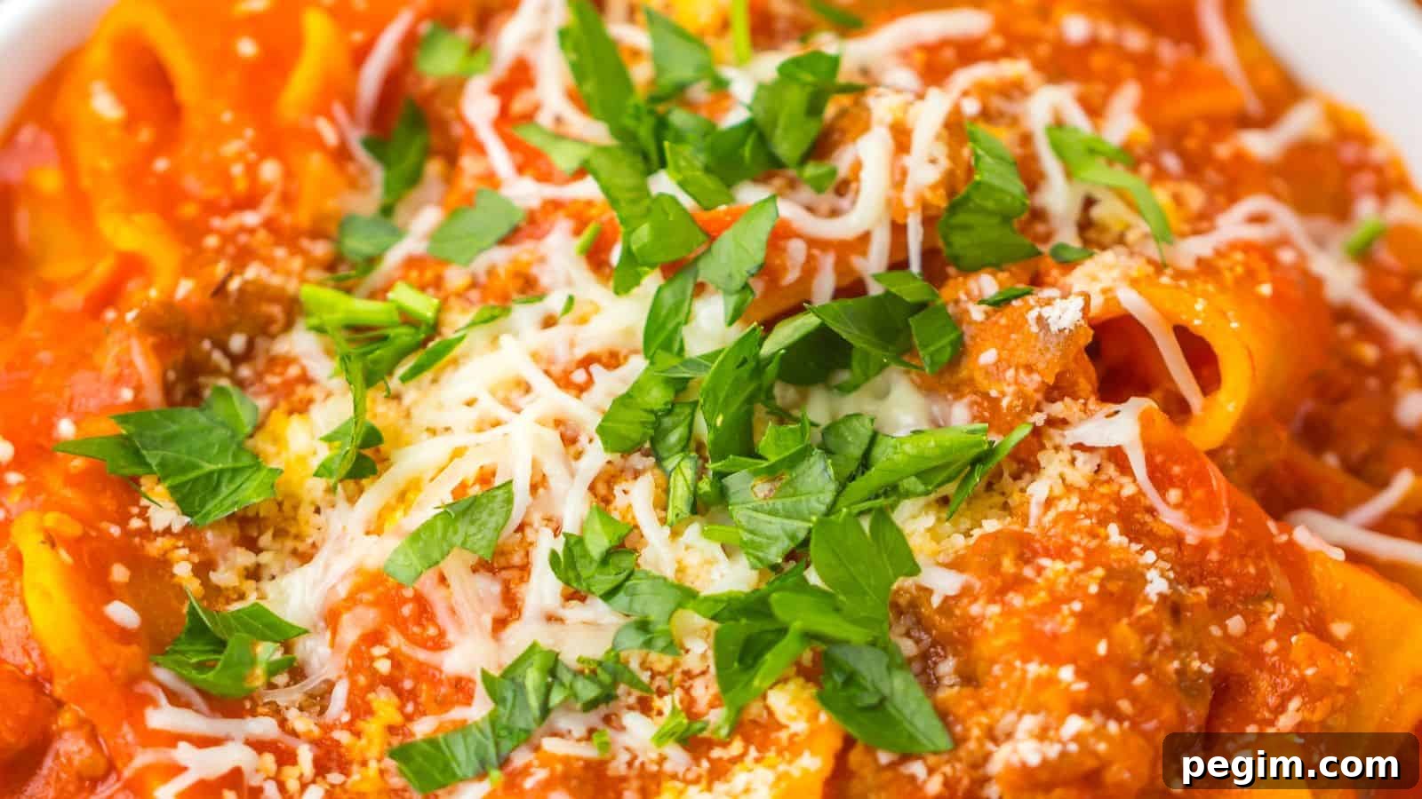 Close-up of a plate of pasta topped with a red tomato-based sauce, grated cheese, and garnished with chopped parsley.